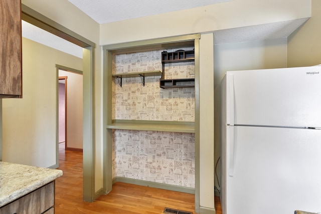 kitchen featuring white refrigerator, light hardwood / wood-style flooring, and a textured ceiling