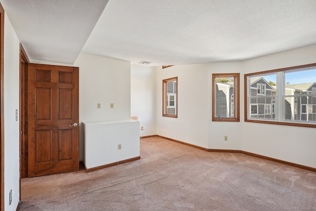 spare room with light carpet, a textured ceiling, visible vents, and baseboards