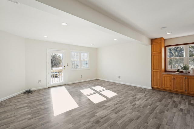 unfurnished living room with recessed lighting, plenty of natural light, wood finished floors, and baseboards