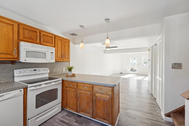 kitchen featuring brown cabinets, visible vents, backsplash, white appliances, and a peninsula