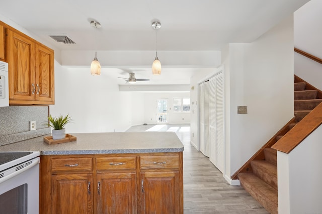 kitchen featuring white appliances, light wood finished floors, visible vents, brown cabinets, and a peninsula