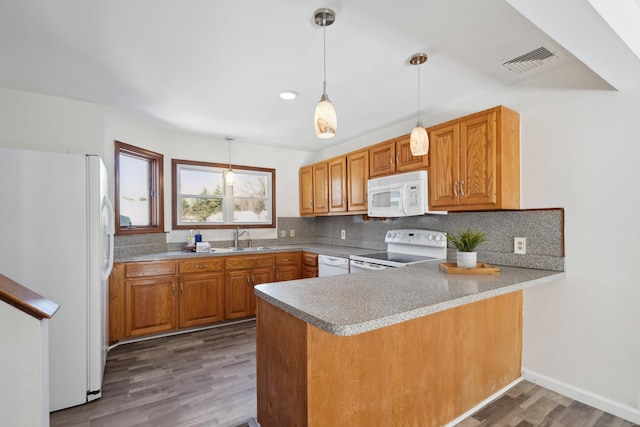 kitchen featuring white appliances, visible vents, a peninsula, a sink, and backsplash