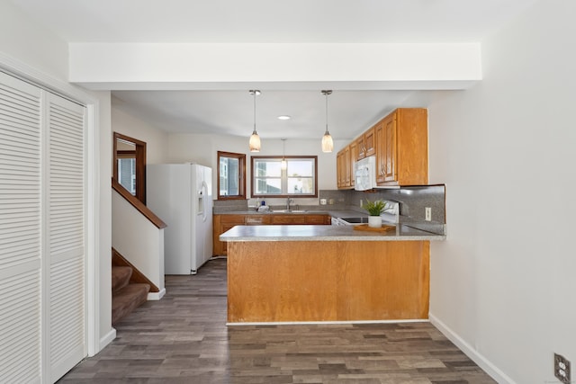 kitchen with white appliances, brown cabinetry, dark wood-type flooring, a peninsula, and backsplash