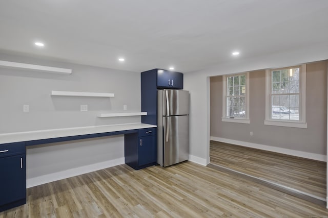 kitchen with light hardwood / wood-style flooring, built in desk, blue cabinetry, and stainless steel refrigerator