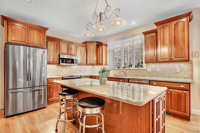 kitchen with stainless steel appliances, pendant lighting, light wood-style flooring, and a center island