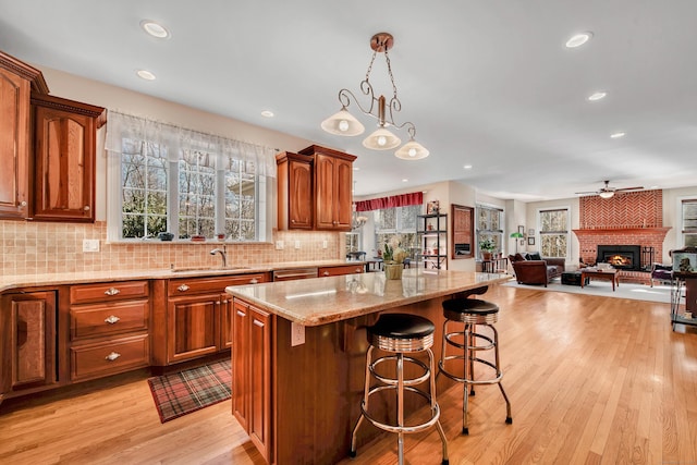 kitchen with light wood finished floors, backsplash, a brick fireplace, light stone countertops, and a sink