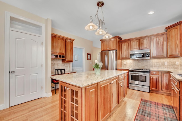 kitchen with tasteful backsplash, a center island, light wood-type flooring, light stone counters, and appliances with stainless steel finishes