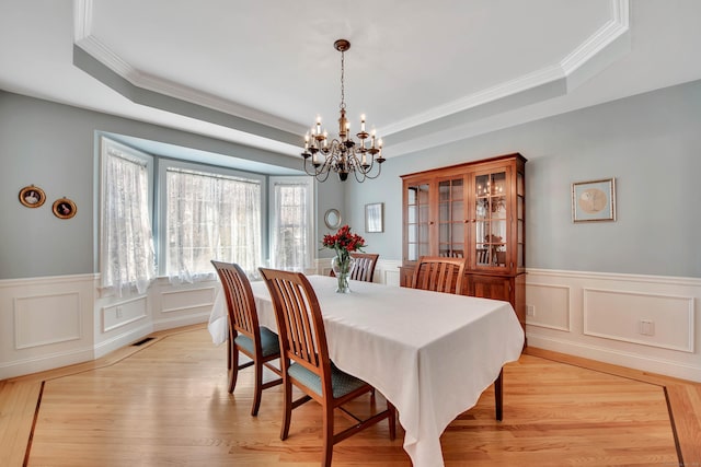 dining space featuring light wood finished floors, a chandelier, a raised ceiling, and visible vents