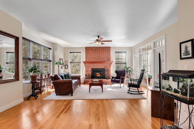 living room featuring ceiling fan, a fireplace, baseboards, and light wood-style floors