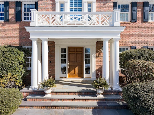 entrance to property with brick siding and a balcony