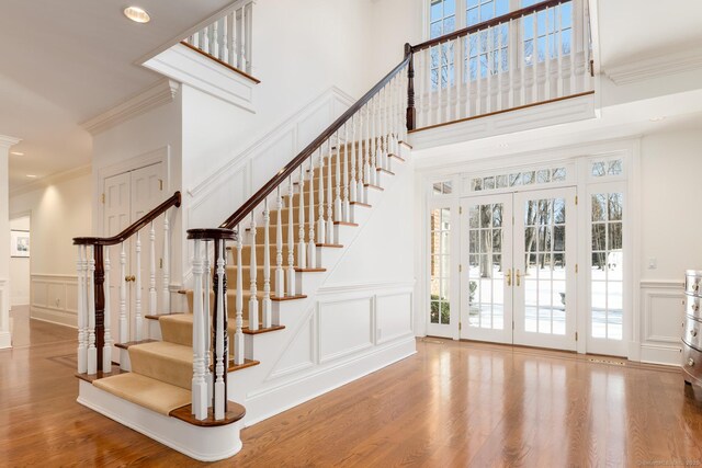 stairway with a wealth of natural light, french doors, a decorative wall, and wood finished floors