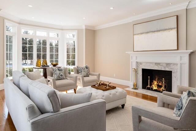 living area featuring baseboards, a premium fireplace, ornamental molding, light wood-type flooring, and recessed lighting