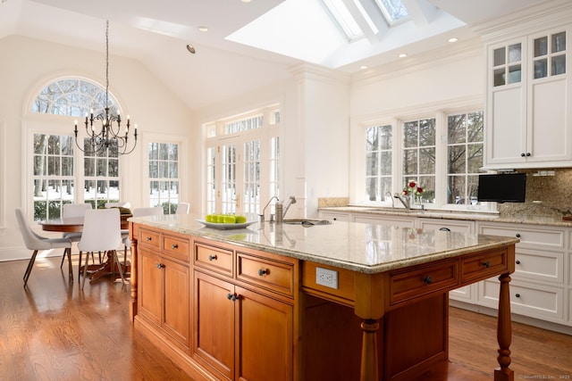 kitchen featuring vaulted ceiling with skylight, light stone countertops, a sink, and wood finished floors