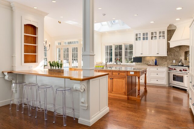 kitchen with a breakfast bar, premium range, a skylight, glass insert cabinets, and custom range hood