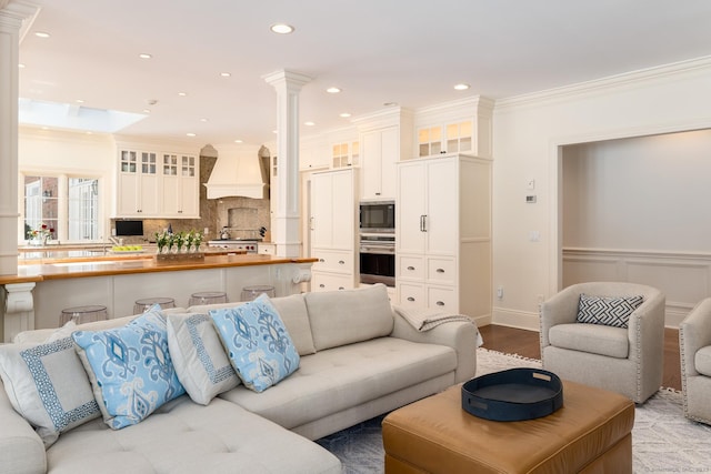 living room with a wainscoted wall, recessed lighting, ornamental molding, wood finished floors, and ornate columns