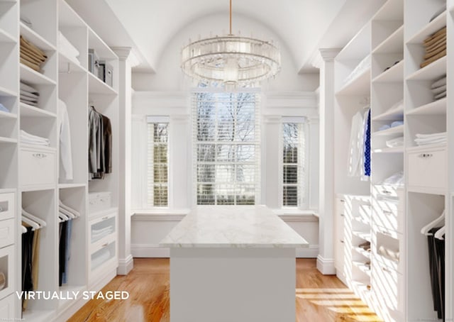 spacious closet with light wood-type flooring, a notable chandelier, and vaulted ceiling