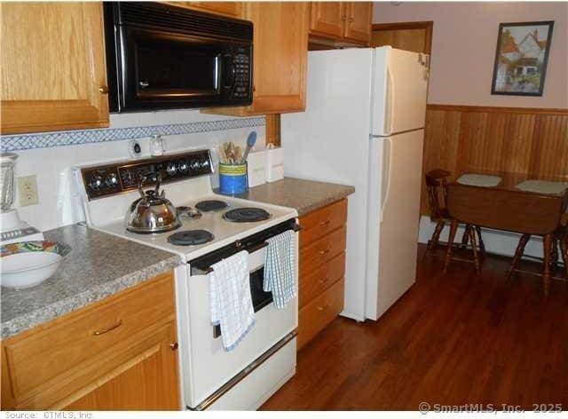 kitchen featuring white appliances, dark hardwood / wood-style flooring, wood walls, and backsplash