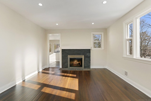 unfurnished living room featuring dark wood-style floors, plenty of natural light, visible vents, and a fireplace with flush hearth