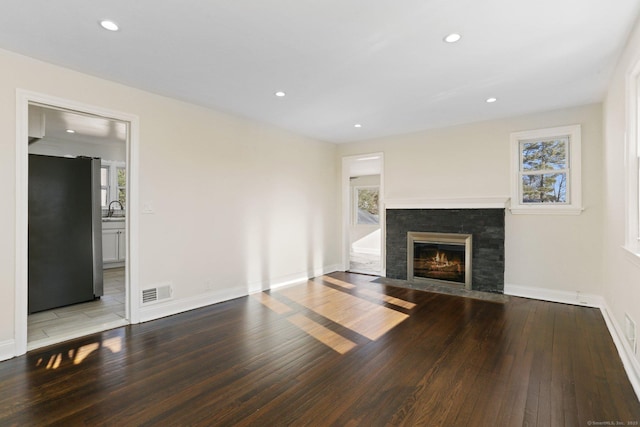 unfurnished living room featuring hardwood / wood-style flooring, recessed lighting, a fireplace with flush hearth, a sink, and visible vents