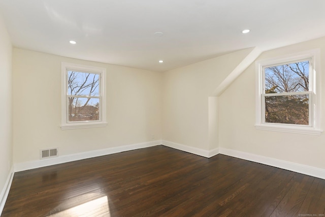 additional living space featuring a healthy amount of sunlight, visible vents, baseboards, and dark wood-style flooring