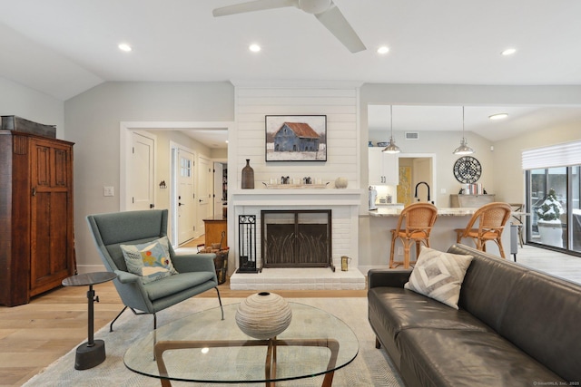 living room with vaulted ceiling, ceiling fan, a fireplace, and light hardwood / wood-style floors