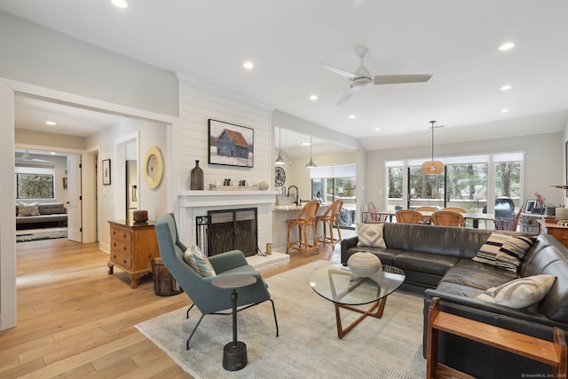 living room with ceiling fan, a brick fireplace, sink, and light wood-type flooring