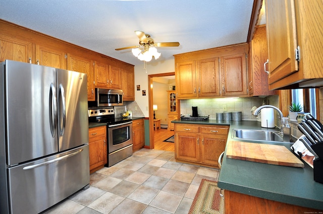 kitchen featuring sink, a baseboard radiator, appliances with stainless steel finishes, ceiling fan, and backsplash