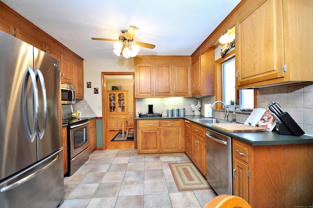 kitchen with light tile patterned flooring, appliances with stainless steel finishes, sink, decorative backsplash, and ceiling fan