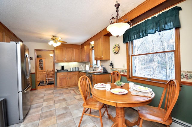 kitchen featuring sink, baseboard heating, appliances with stainless steel finishes, hanging light fixtures, and a textured ceiling