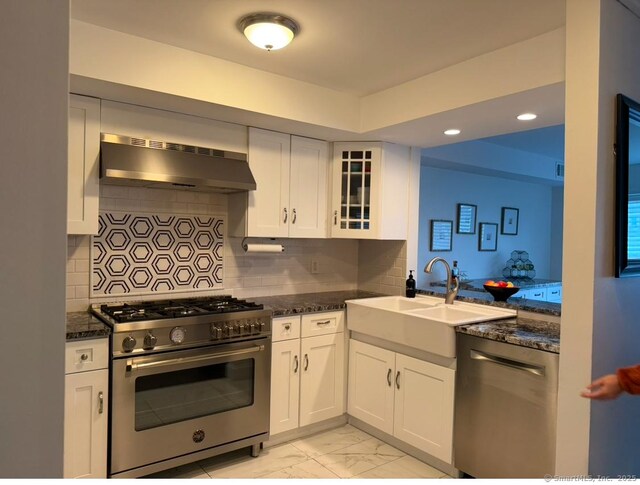 kitchen with appliances with stainless steel finishes, ventilation hood, white cabinetry, sink, and dark stone countertops