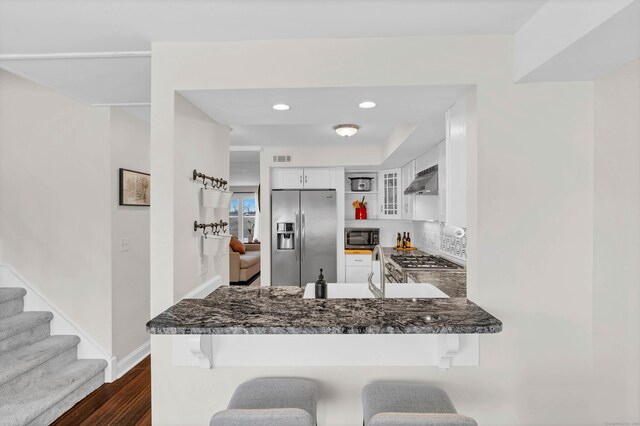 kitchen with tasteful backsplash, white cabinets, a kitchen bar, kitchen peninsula, and stainless steel appliances