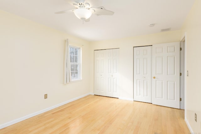 unfurnished bedroom with ceiling fan, light hardwood / wood-style floors, and multiple closets