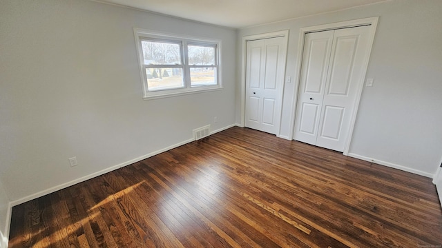 unfurnished bedroom with dark hardwood / wood-style flooring and multiple closets