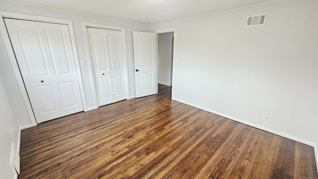 unfurnished bedroom with multiple closets and dark wood-type flooring