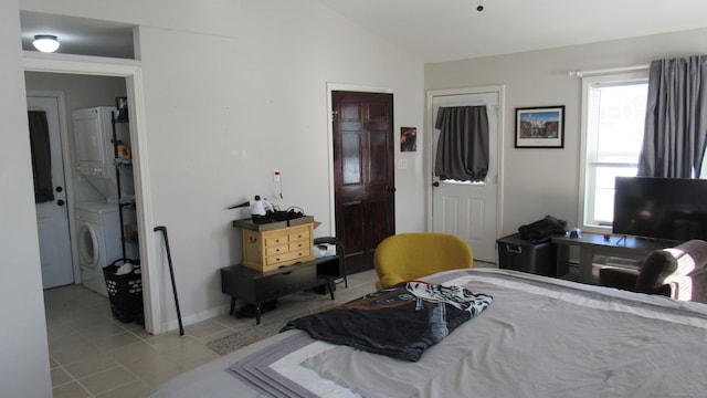 bedroom featuring lofted ceiling, stacked washing maching and dryer, and light tile patterned floors