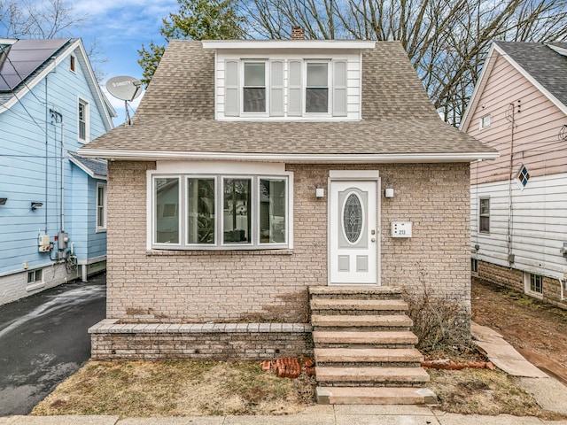 view of front facade featuring a shingled roof, brick siding, driveway, and a chimney