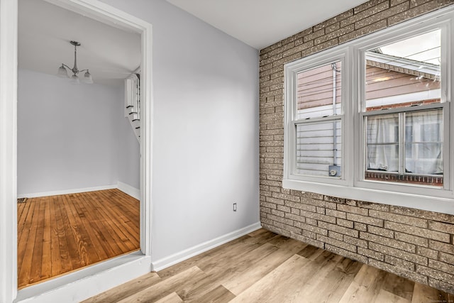 spare room featuring brick wall, a notable chandelier, baseboards, and wood finished floors