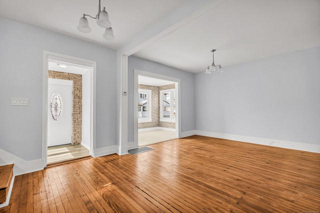 interior space featuring baseboards, visible vents, wood-type flooring, brick wall, and a notable chandelier