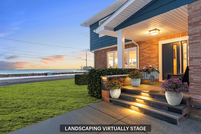 patio terrace at dusk with a lawn, a porch, and a water view