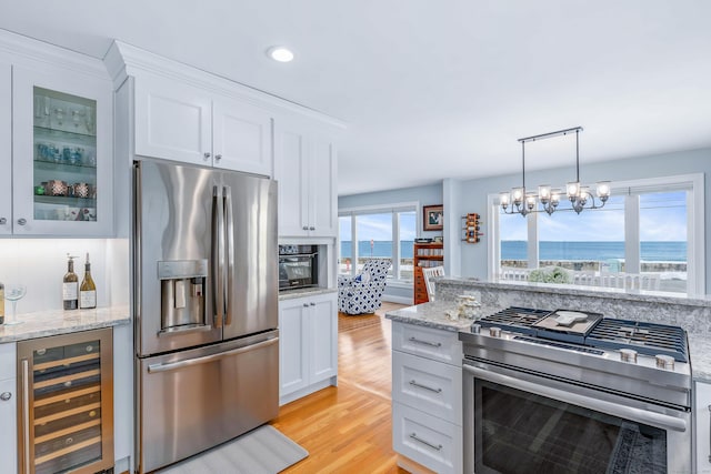 kitchen with stainless steel appliances, a water view, wine cooler, light stone countertops, and white cabinets