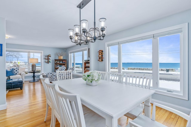 dining area with a view of the beach, light wood-type flooring, a healthy amount of sunlight, and a water view