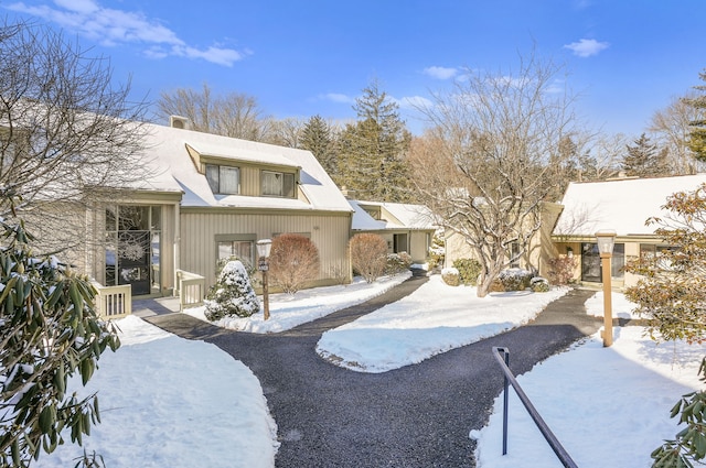 snow covered property featuring driveway and a chimney