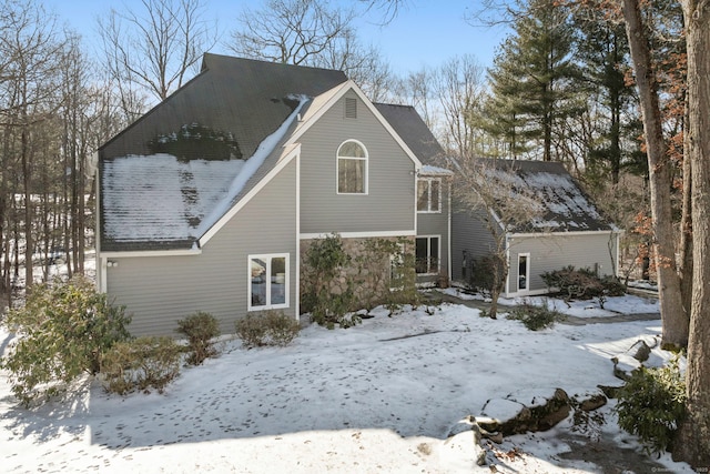 snow covered back of property featuring stone siding