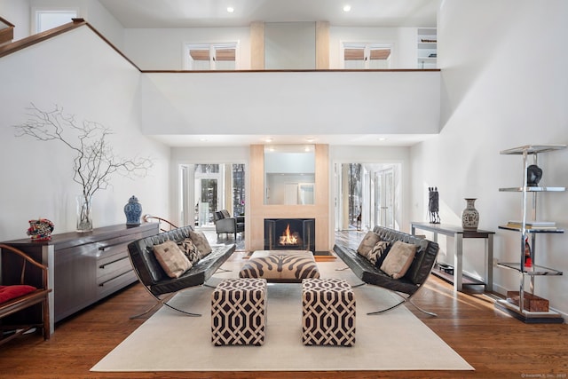 living area with recessed lighting, dark wood finished floors, a lit fireplace, and a high ceiling