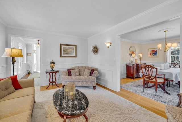 living area featuring a wainscoted wall, light wood-style flooring, a chandelier, and crown molding