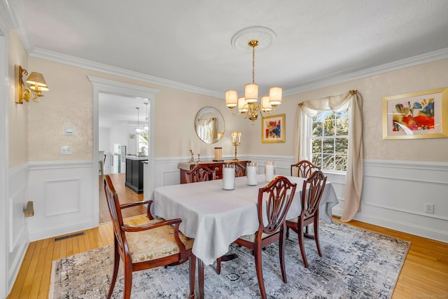 dining room with ornamental molding, wainscoting, a notable chandelier, and light wood-style flooring