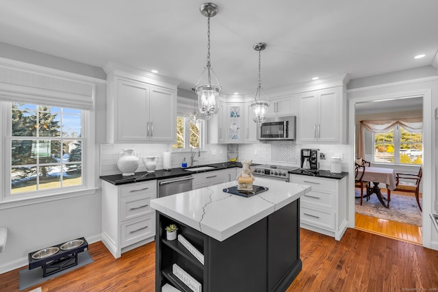 kitchen with pendant lighting, stainless steel appliances, white cabinets, a kitchen island, and a sink