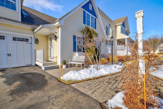 view of snowy exterior with a garage, aphalt driveway, and roof with shingles