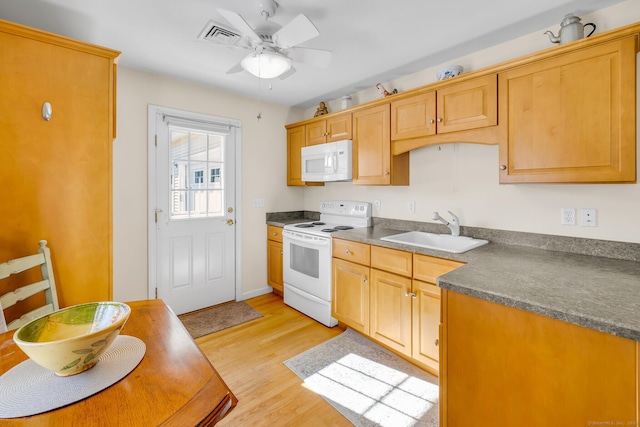 kitchen featuring white appliances, a sink, a ceiling fan, light wood-style floors, and dark countertops