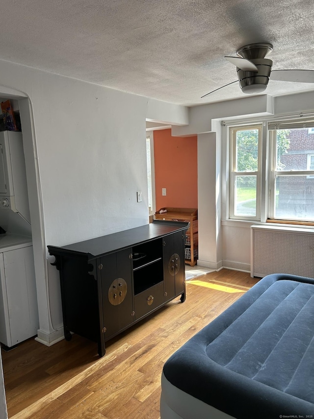 bedroom with radiator heating unit, stacked washer and clothes dryer, ceiling fan, a textured ceiling, and light hardwood / wood-style flooring